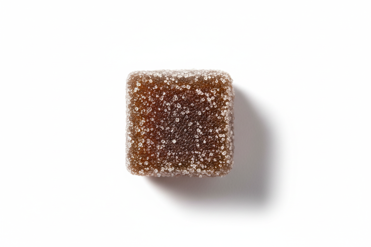 single sugar-coated dark brown cubed gummy overhead casting a light shadow isolated on white
